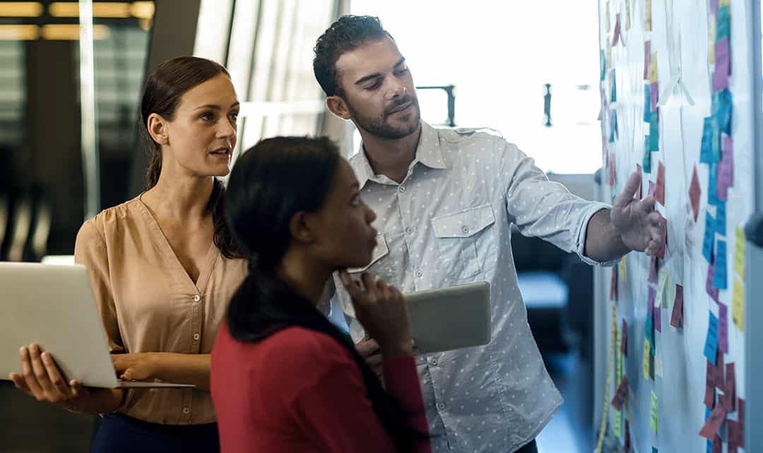 A work team looks over sticky notes on a visual management board