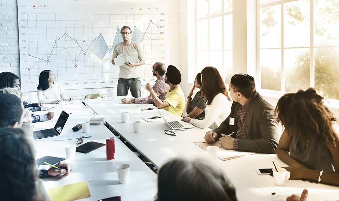 A man wearing glasses presents to a diverse set of co-workers during a meeting