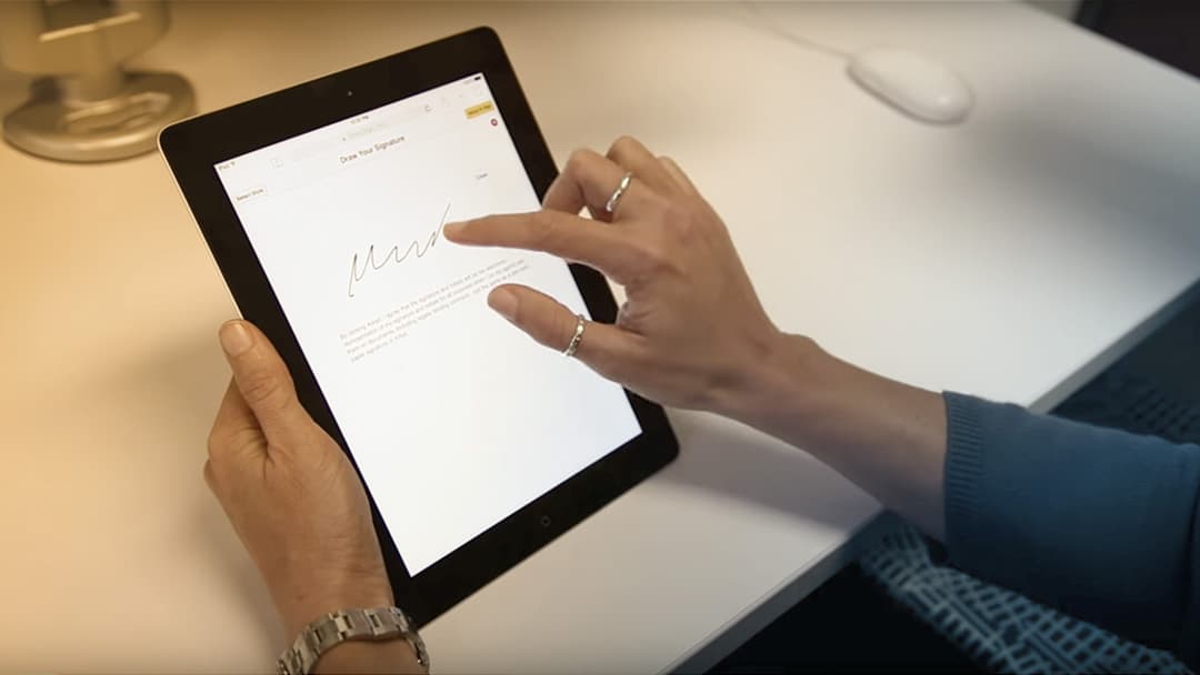 A woman signs a digital document on a tablet computer.